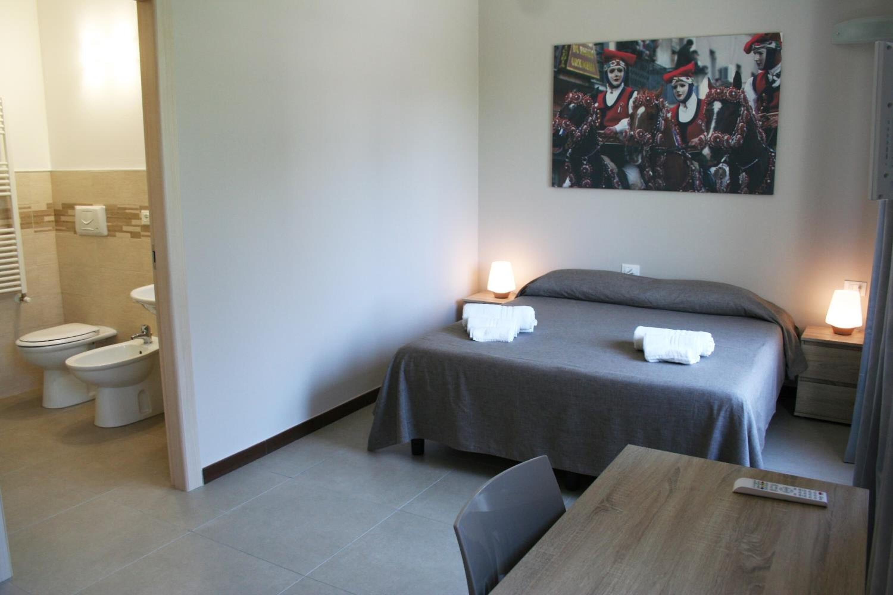 Una habitación de hotel con cama, dos lámparas de noche, una mesa, una silla, un inodoro y un bidé.