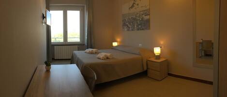 A hotel room with a bed, bedside tables, a desk, a window with curtains, and a wall-mounted picture.