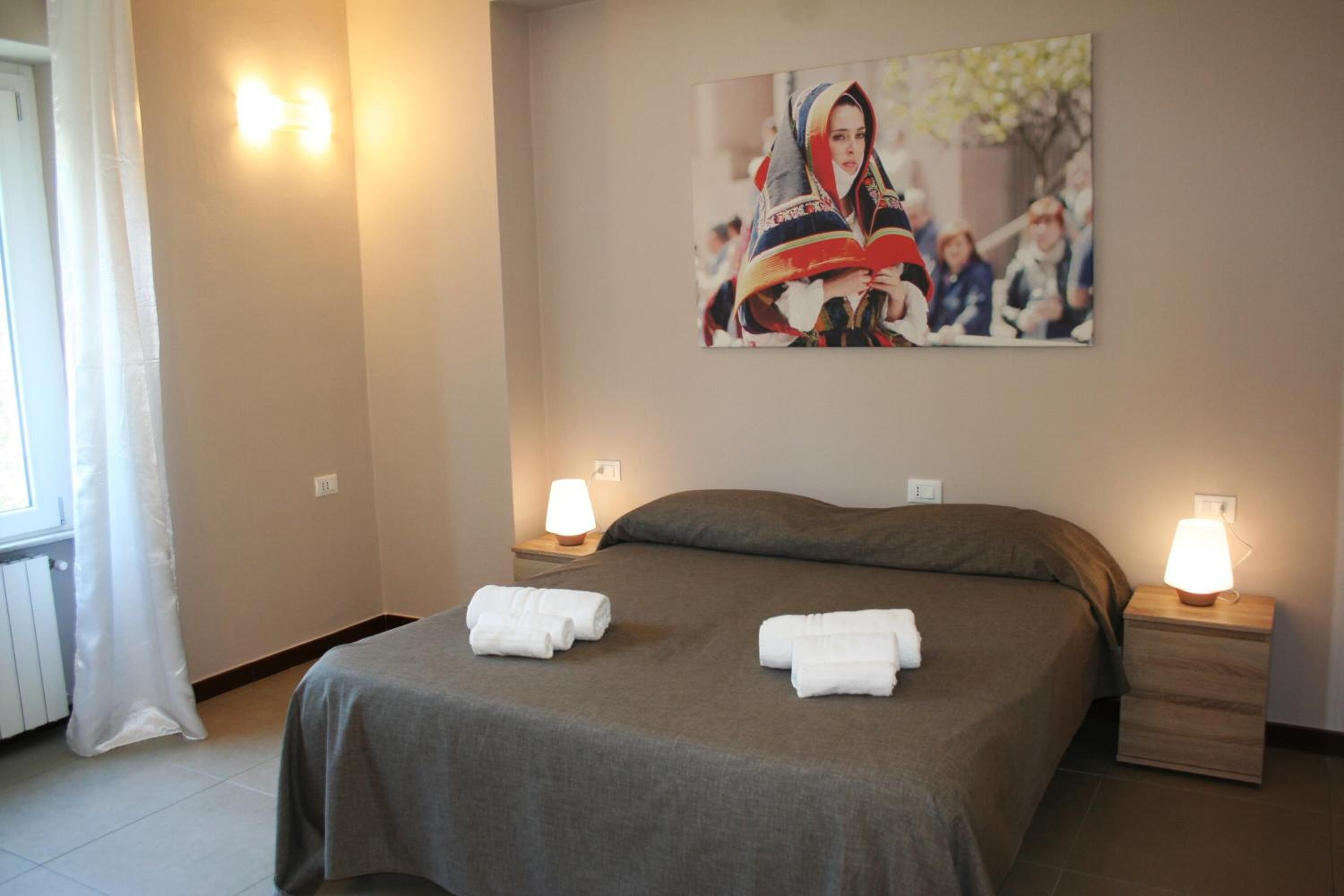 A hotel room with a bed, two bedside lamps, a painting on the wall, and a window with curtains.