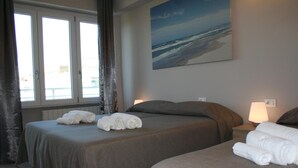 Een hotelkamer met twee bedden, een schilderij van een strand en een raam met gordijnen.