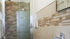 Een moderne badkamer met een douche met glazen wand, een groot wastafel en een bidet.