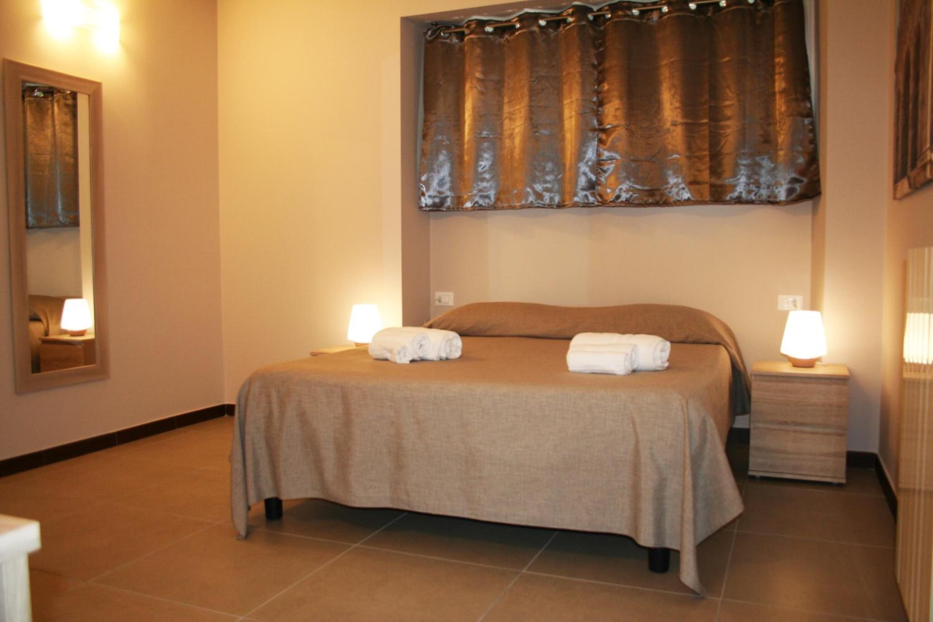 Una cama bien hecha con una colcha color beige y dos almohadas, flanqueada por mesitas de noche con lámparas.