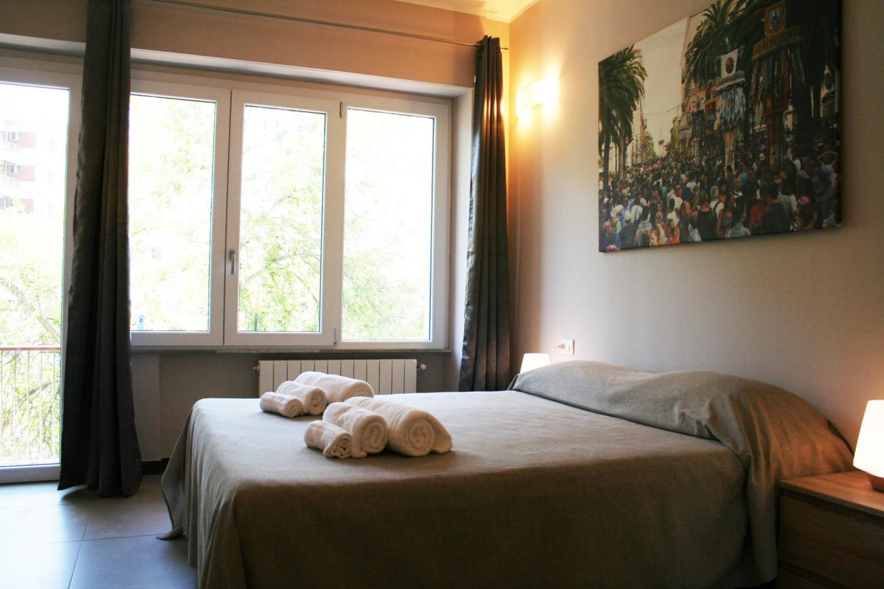 Ein Hotelzimmer mit Bett, Nachttisch, einem Bild an der Wand und einem Fenster mit Vorhängen.