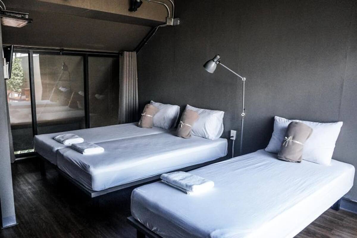 A modern hotel room with two single beds, a bedside table with a lamp, and a large window with curtains.