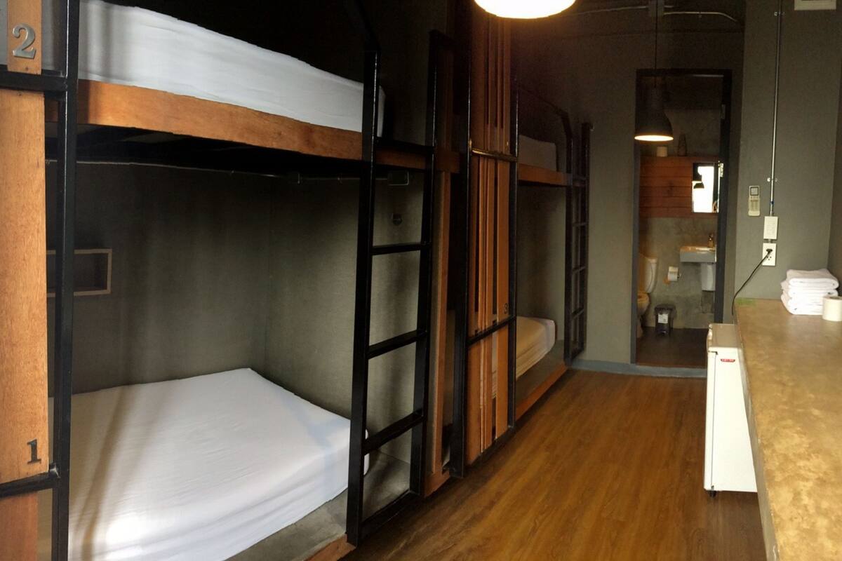 A bunk bed room with a wooden floor, a small desk, and a bathroom with a toilet and sink.