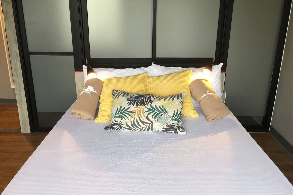 A neatly made bed with a white mattress, a yellow knitted throw blanket, and two beige pillows.