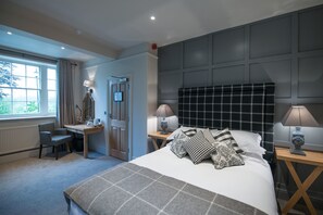 A bedroom with a bed, two bedside tables with lamps, a desk with a chair, a window with curtains, and a door.