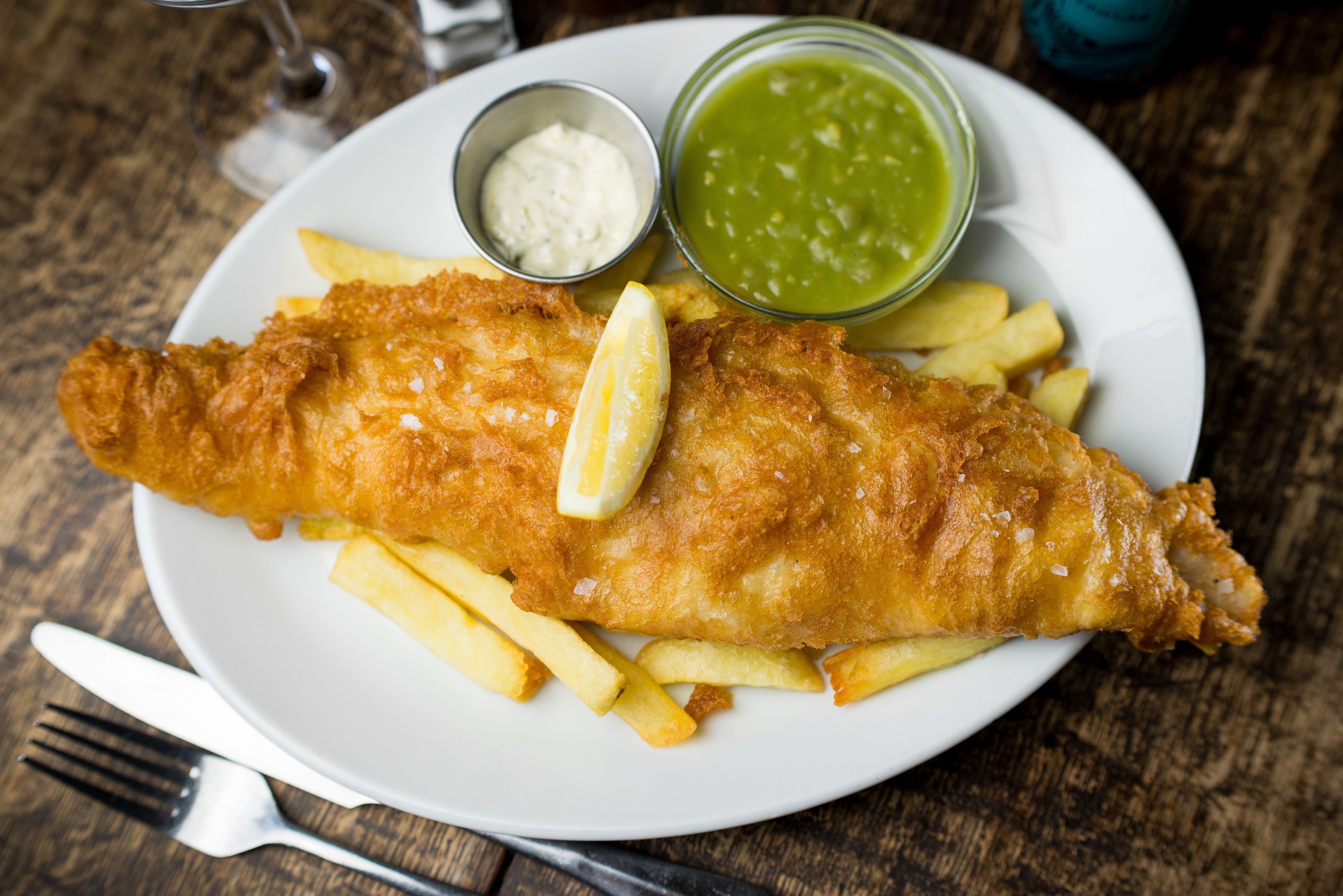 A plate with fish and chips, lemon wedges, and two sauces.