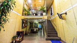 A hotel lobby with a staircase, a reception desk, and potted plants.