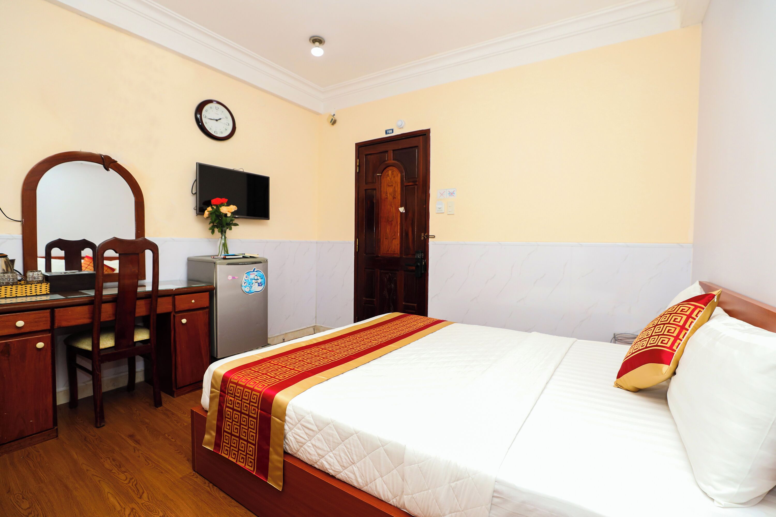 A hotel room with a bed, a desk with a chair, a television, and a clock on the wall.