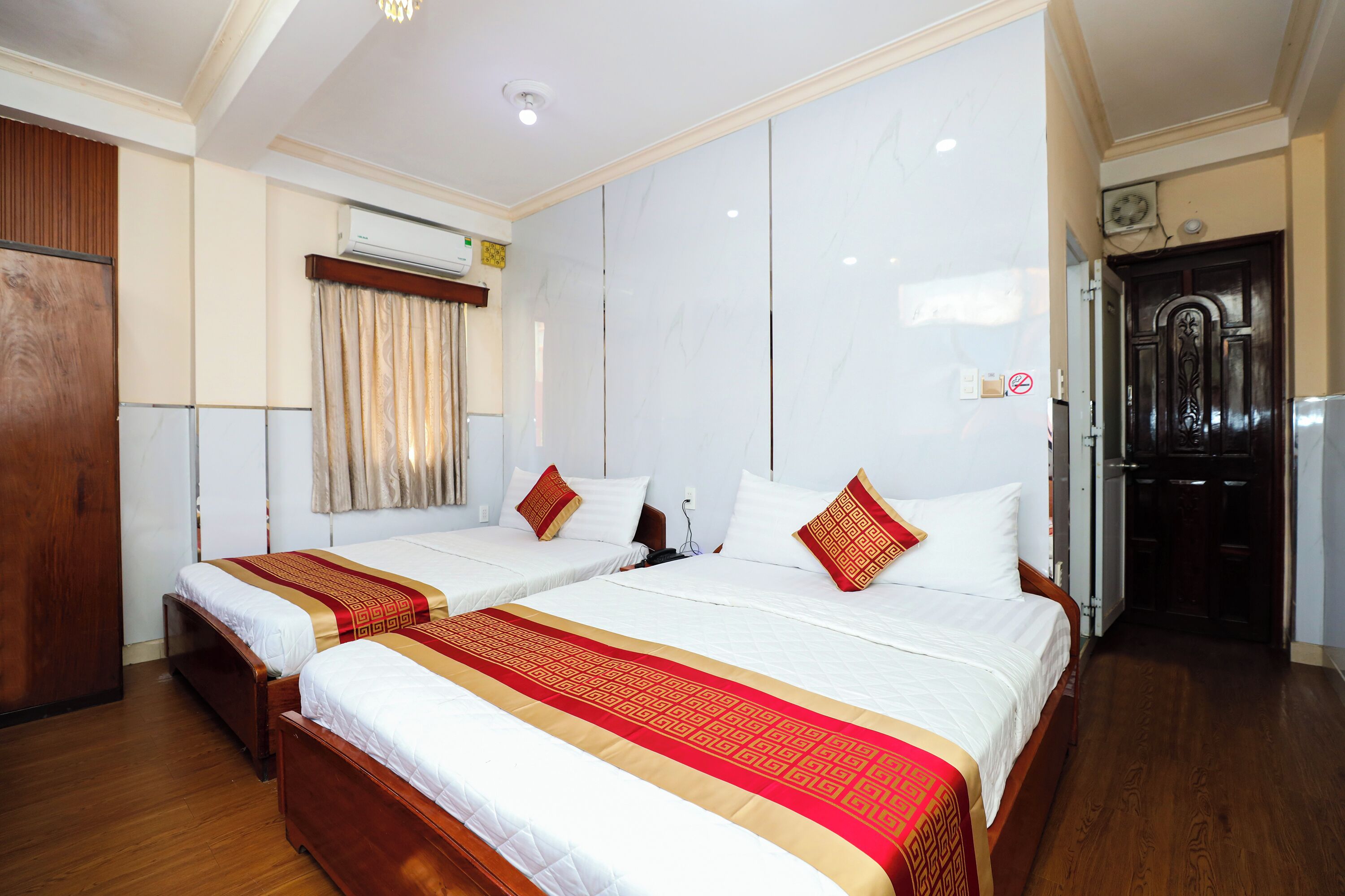 A hotel room with two beds, wooden flooring, a wardrobe, an air conditioning unit, and a door with a sign.