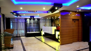 Un moderno vestíbulo de hotel con mostrador de recepción, suelo de mármol e iluminación LED azul.