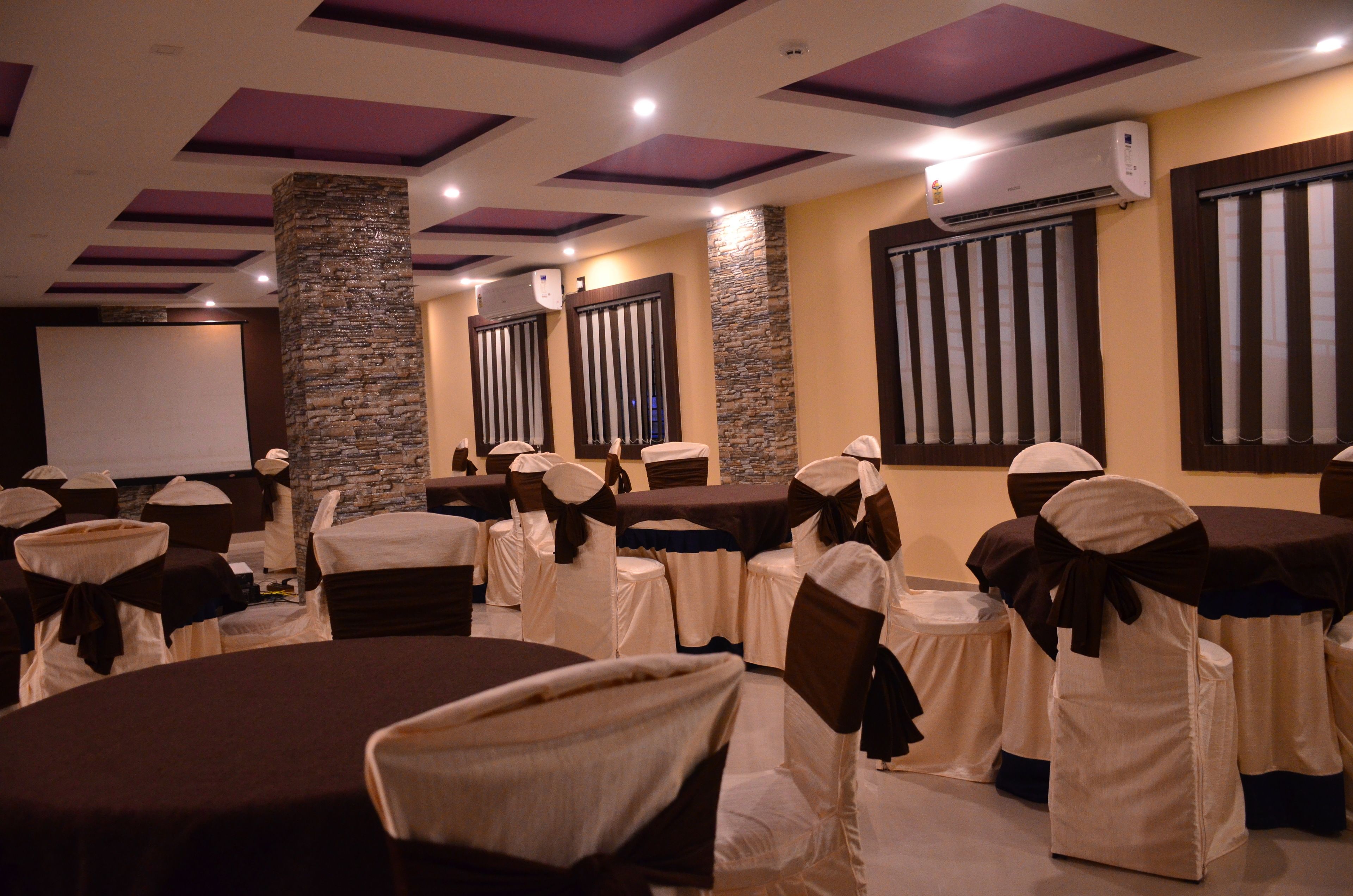 A conference room with tables and chairs, air conditioning units, and a projector screen.
