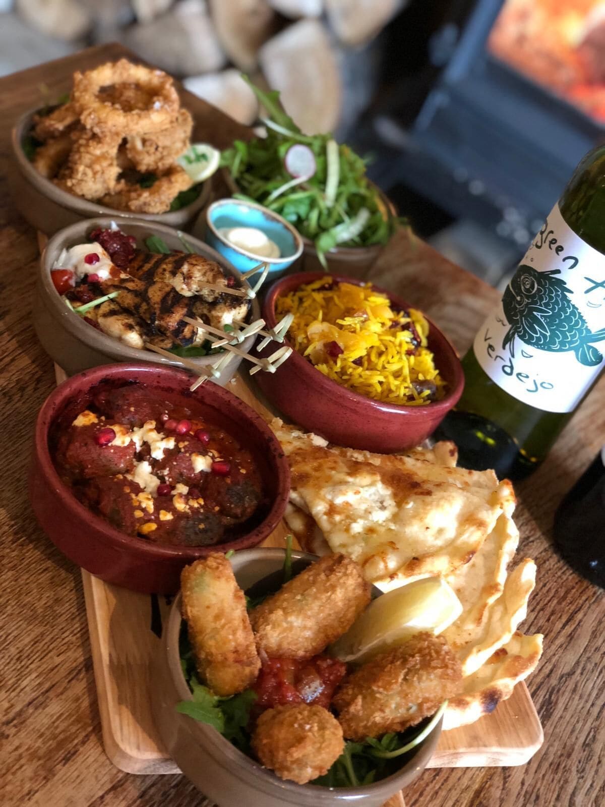 A wooden table with various dishes including fried items, a bowl of rice, and a bottle of wine.