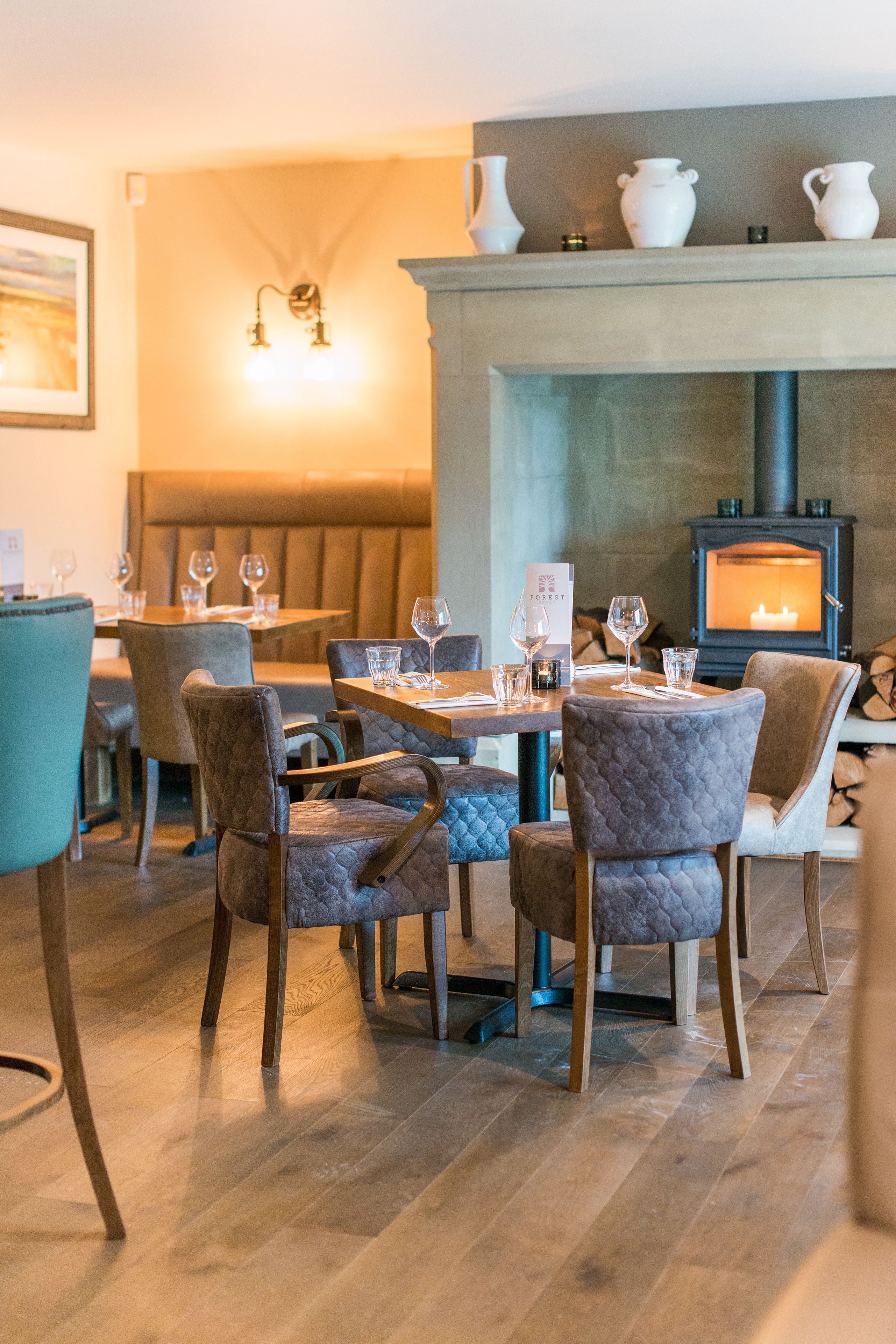 A cozy restaurant with wooden tables and cushioned chairs, a fireplace, and a stone wall.