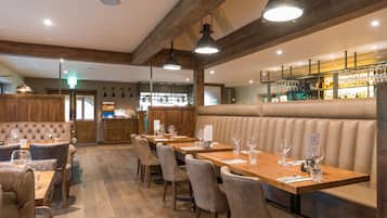 A restaurant with wooden beams, leather booths, and a bar area.