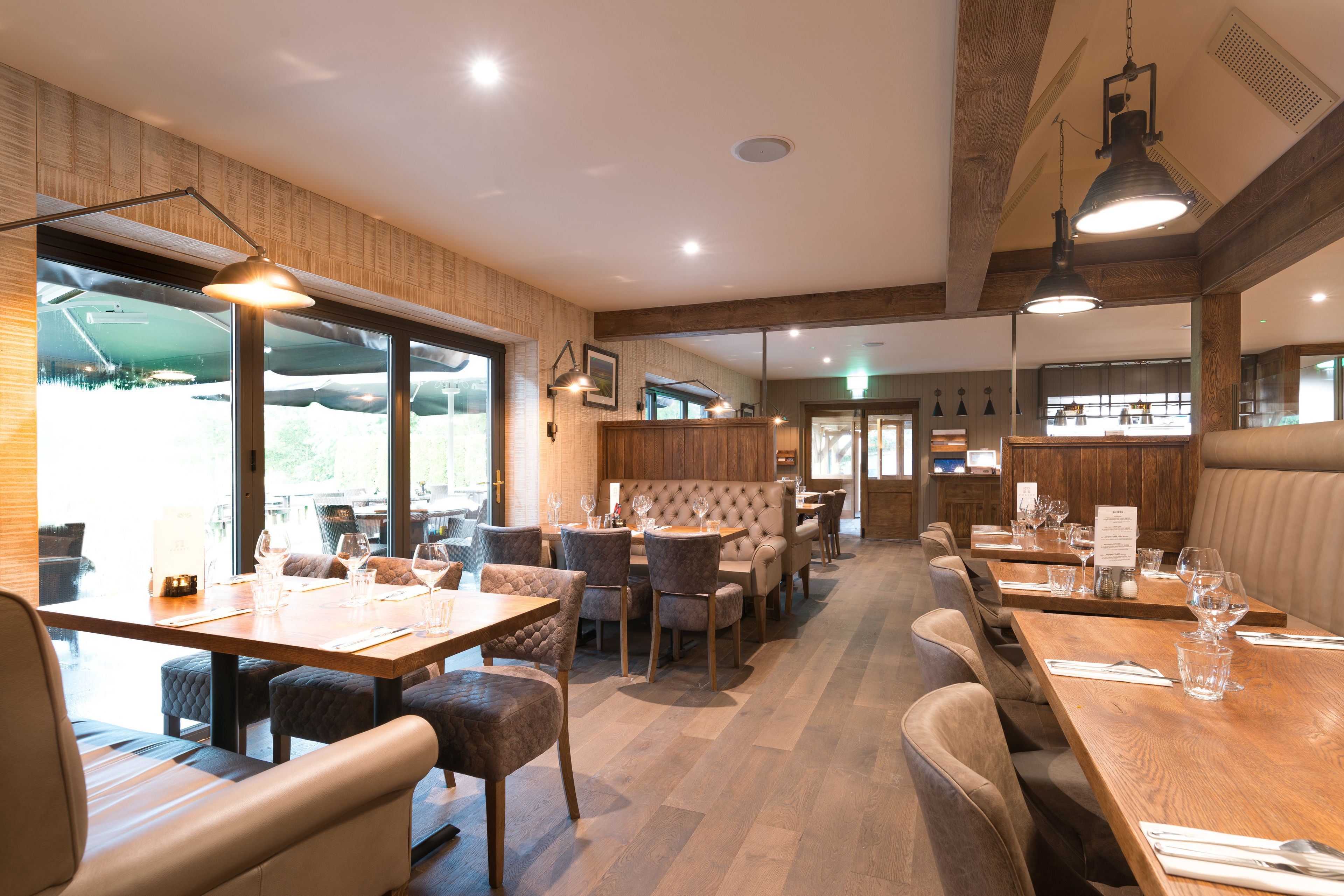 A restaurant with wooden tables, cushioned chairs, and pendant lighting.