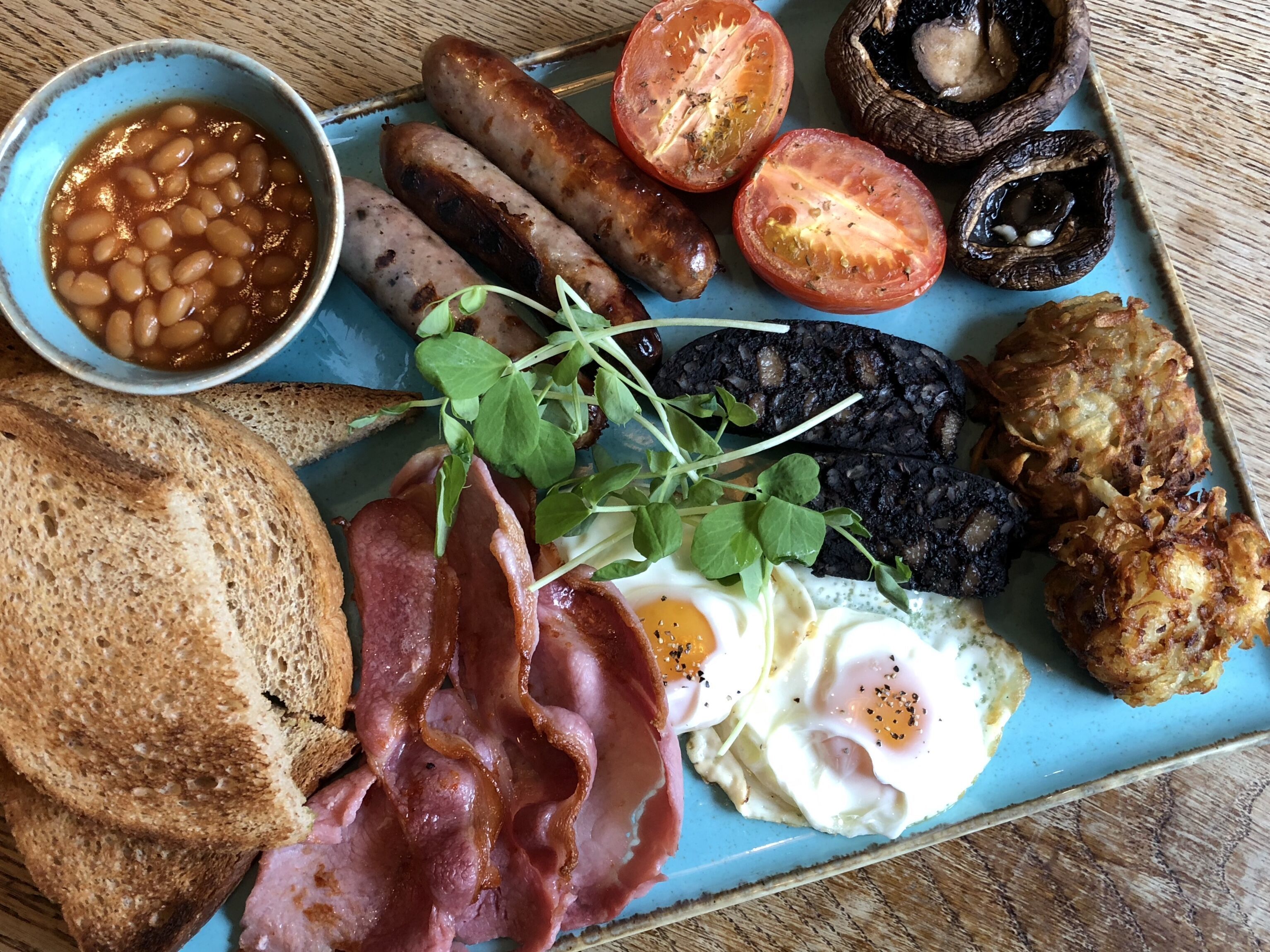 Un plato de desayuno con huevos, tocino, salchichas, frijoles, tomates, champiñones y tostadas.