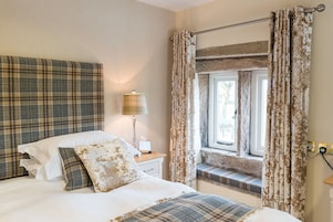 Un dormitorio con cama, lámpara de noche, ventana con cortinas y vistas al exterior.