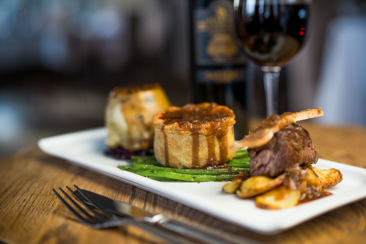 A plate with food and a glass of red wine on a wooden table.