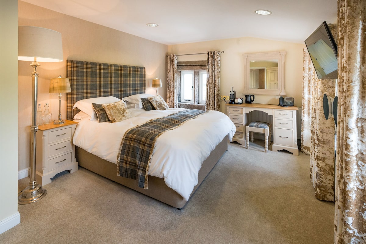 A bedroom with a bed, bedside tables, a desk, a chair, a mirror, and a television.