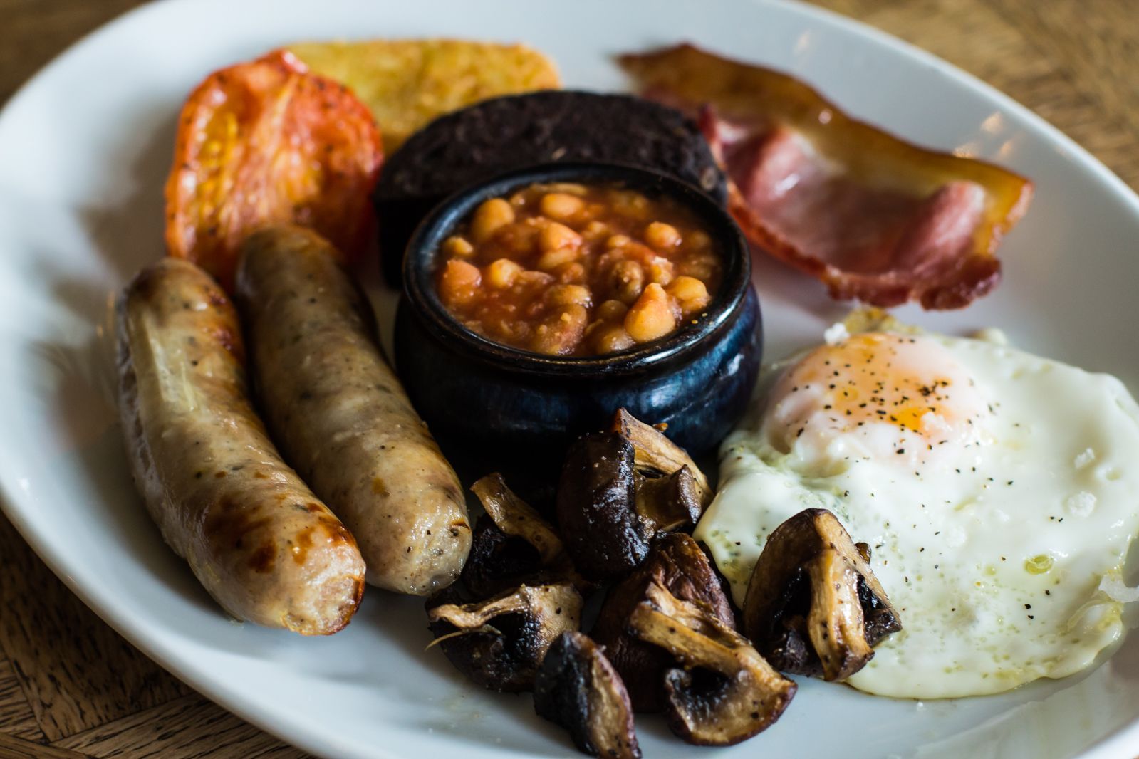 A plate of breakfast food including sausages, mushrooms, beans, bacon, and a fried egg.