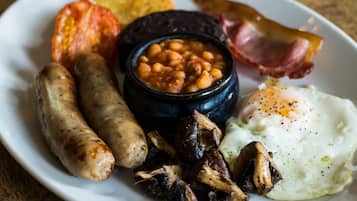 A plate of breakfast food including sausages, mushrooms, beans, bacon, and a fried egg.