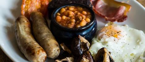 Un plato de comida para el desayuno con salchichas, champiñones, frijoles, tocino y un huevo frito.