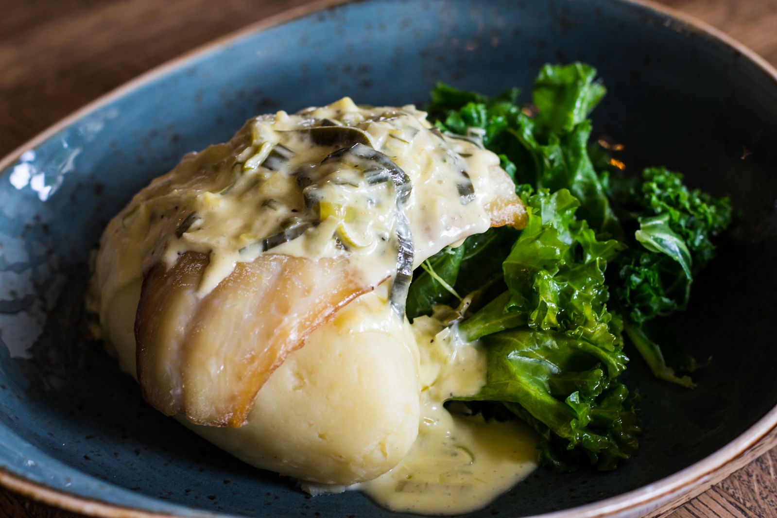 Ein Teller mit Fisch, bedeckt mit cremiger Soße, dazu grünes Gemüse.