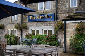 The Alma Inn, a stone building with a signboard, outdoor seating, and flower boxes.