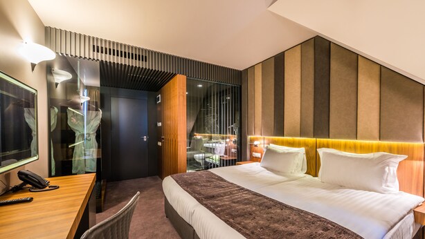 A modern hotel room with a large bed, a desk with a telephone, and a glass partition separating the room from a dining area. - All Seasons Residence Hotel (Sofia)