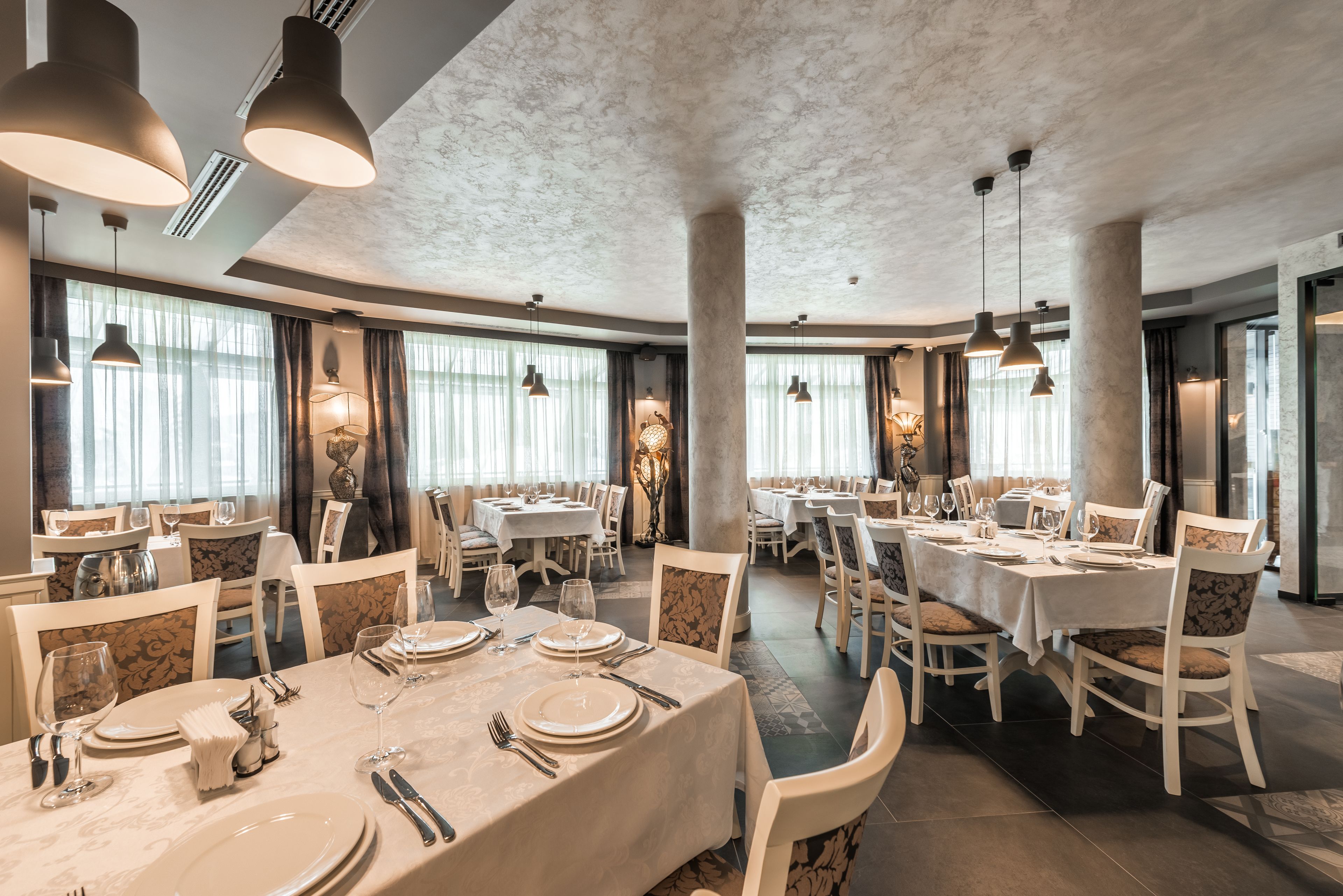 A spacious dining area with multiple tables and chairs, large pendant lights, and a marble ceiling.