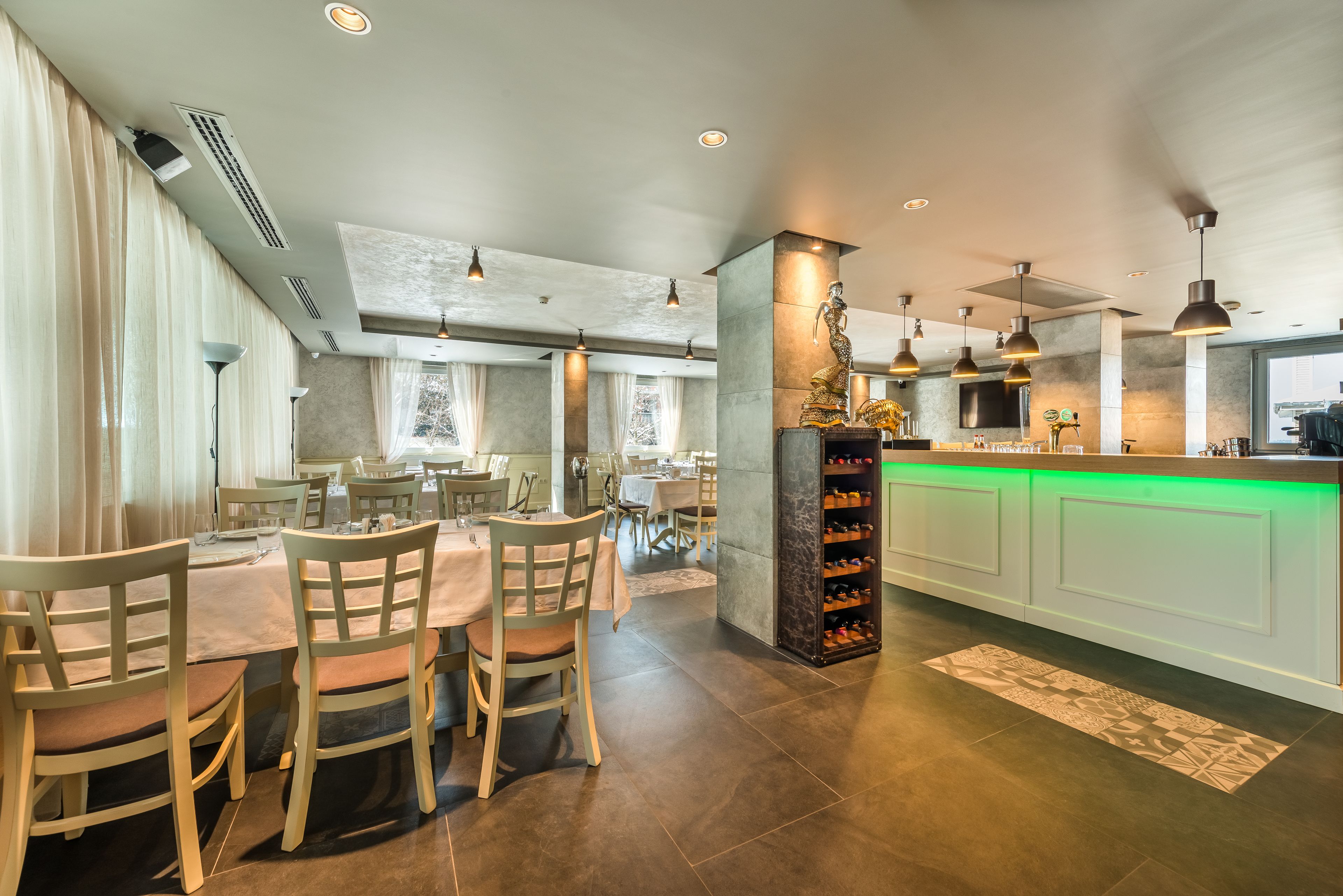 Un espace repas moderne avec une table centrale, des chaises et un coin bar doté d’un comptoir éclairé de lumière verte.