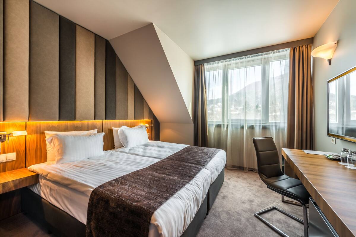 A modern hotel room with a large bed, a desk, and a chair.
