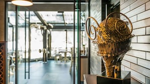 A metal sculpture on a wooden platform in a modern interior space with glass doors leading to a dining area. - All Seasons Residence Hotel (Sofia)
