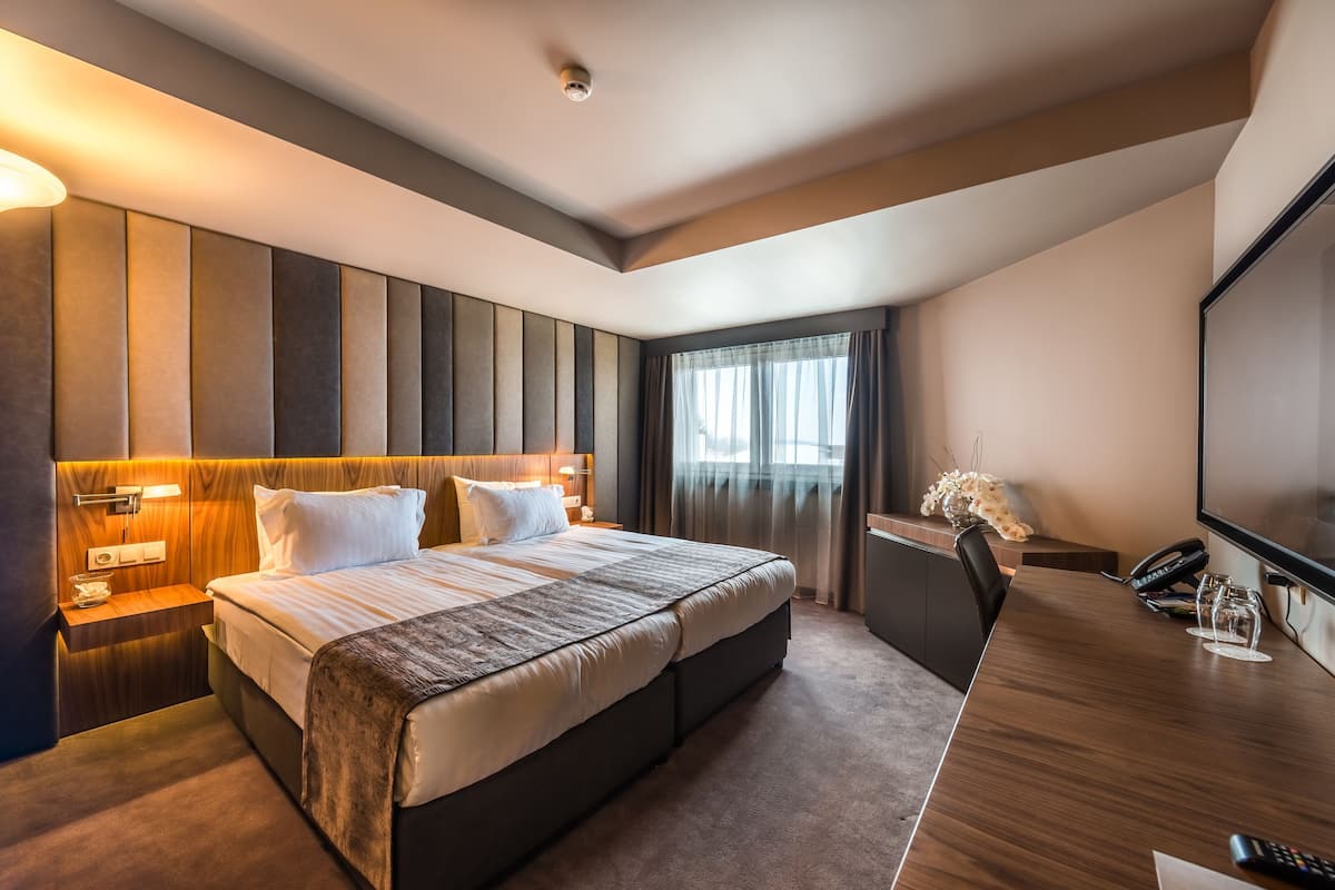 A modern hotel room with a large bed, bedside tables, a desk, and a flat-screen TV.