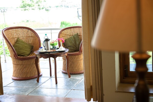 Une pièce comprenant deux fauteuils en osier, une petite table avec une bouteille d’eau, un vase de fleurs et une lampe.