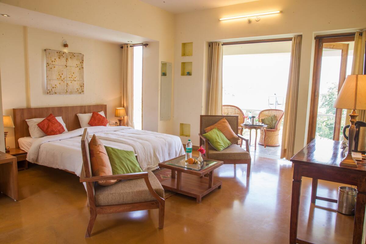 A hotel room with a large bed, two chairs, a small table, and a desk with a lamp.