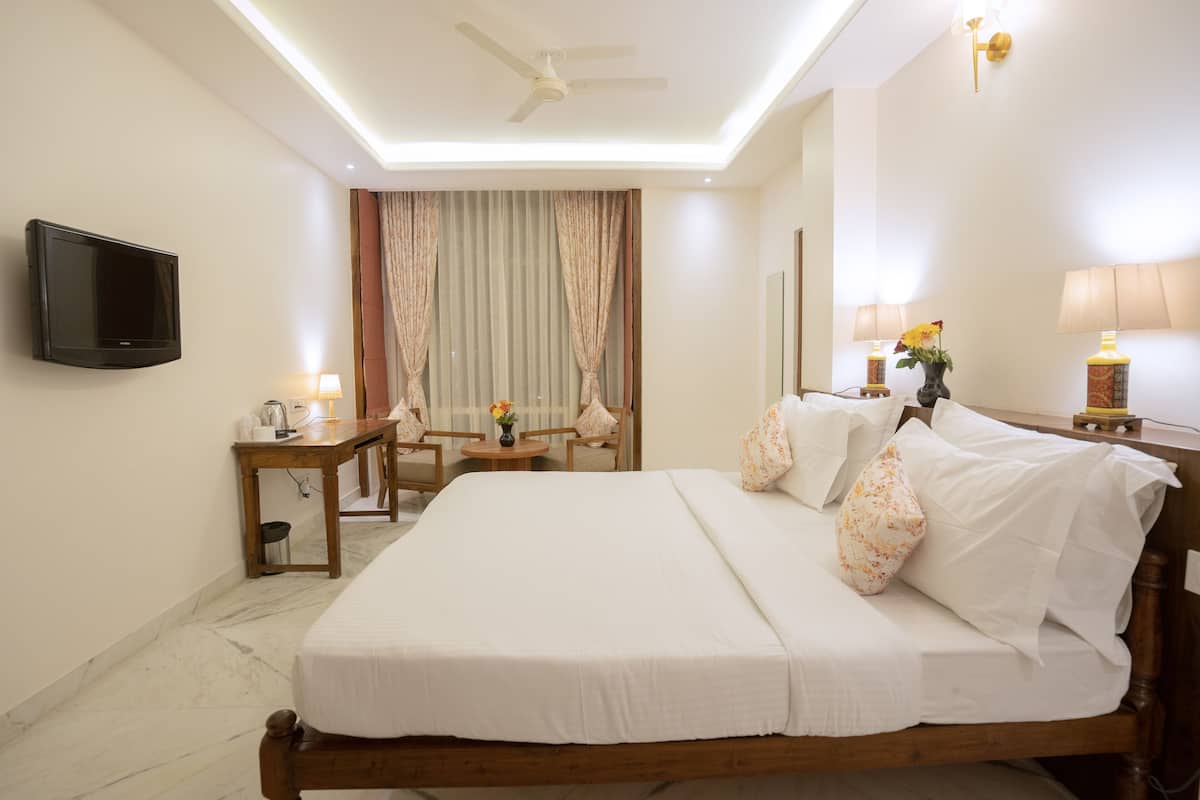 A hotel room with a large bed, a flat-screen TV, a ceiling fan, a desk with a lamp, and a window with curtains.