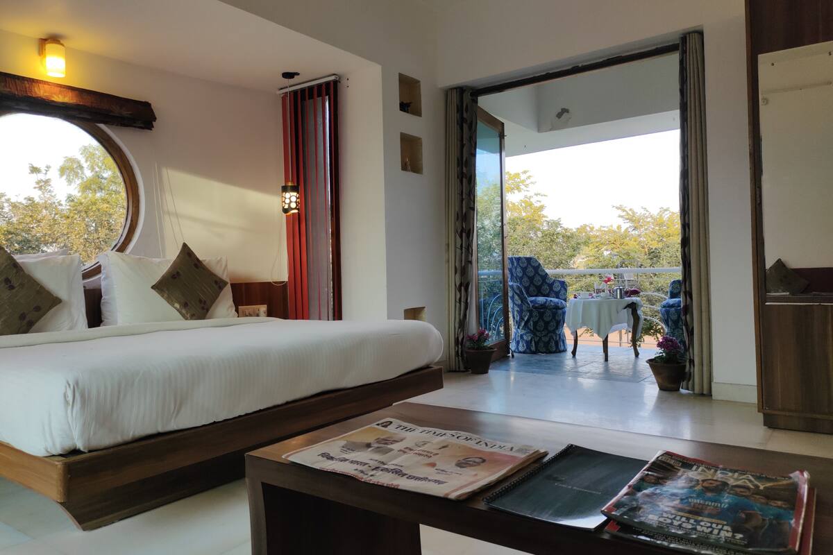 A hotel room with a bed, a table with newspapers, and a view of the outside.