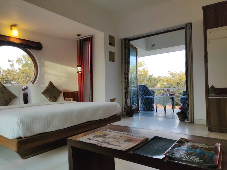 A hotel room with a bed, a table with newspapers, and a view of the outside.