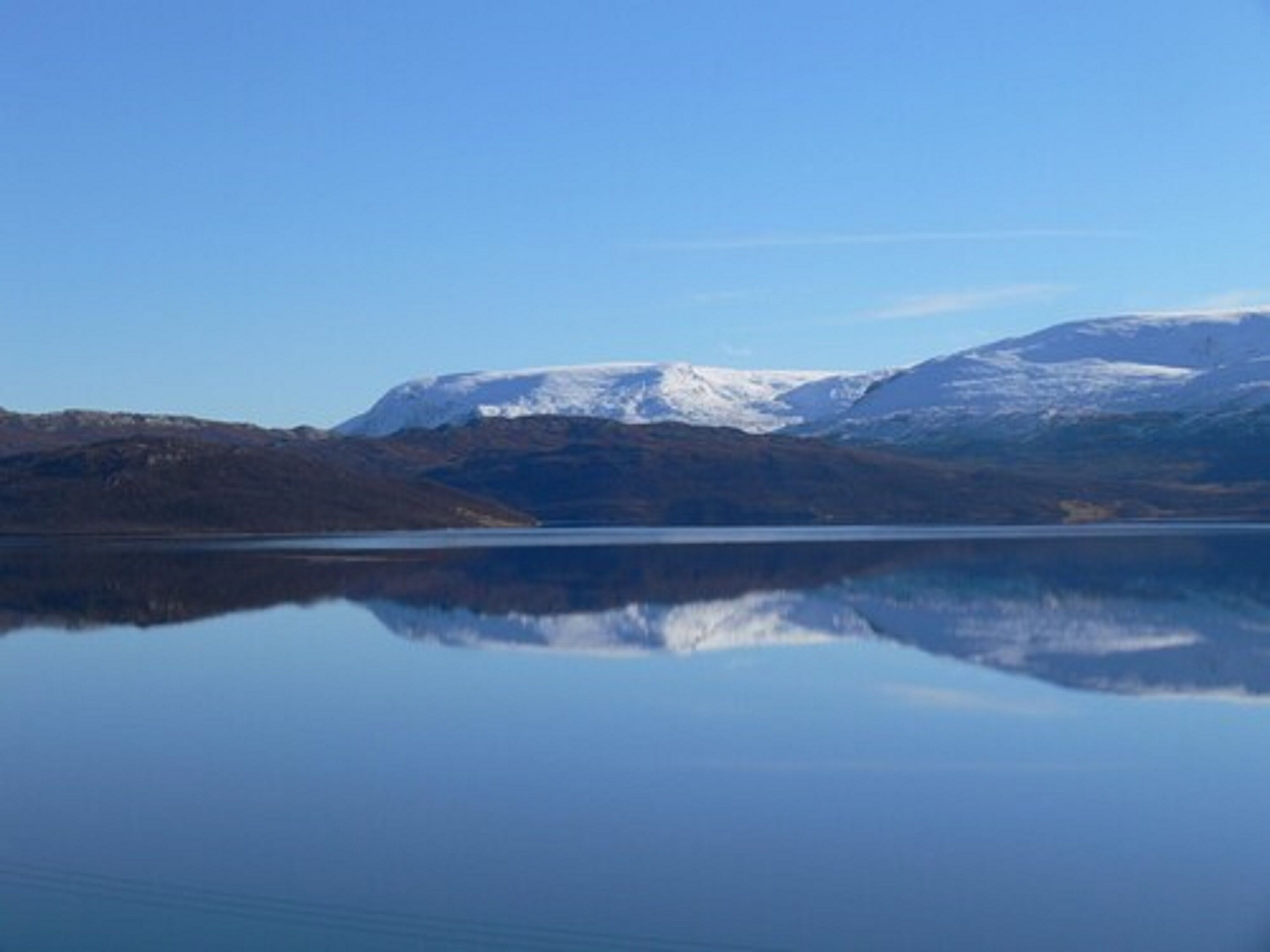 A calm lake reflecting snow-capped mountains under a clear sky.