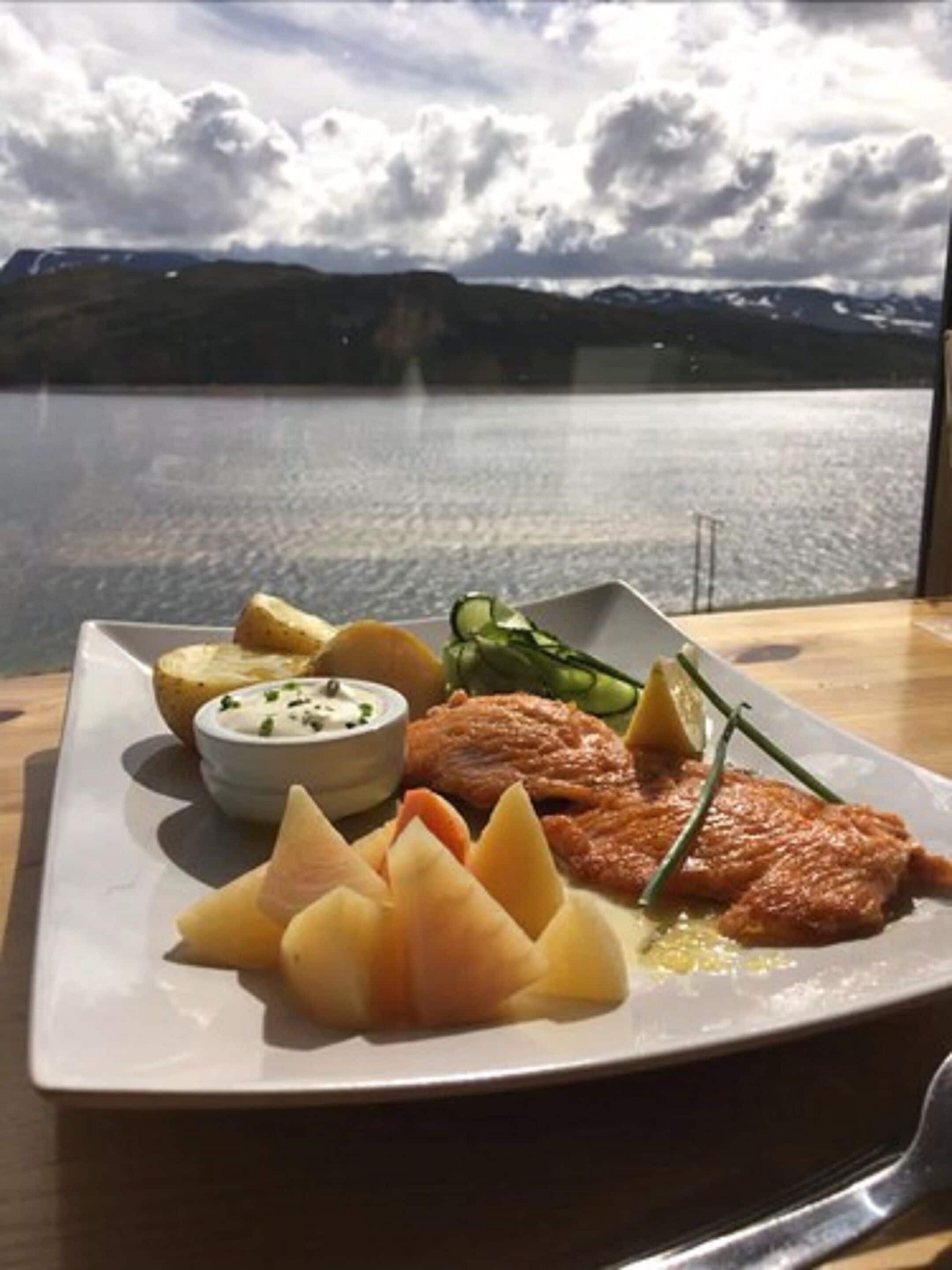 A plate of food with a view of a lake and mountains in the background.