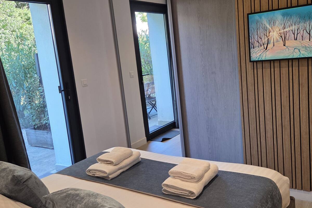 A hotel room with a bed, a TV mounted on the wall, and a view of the outdoors.