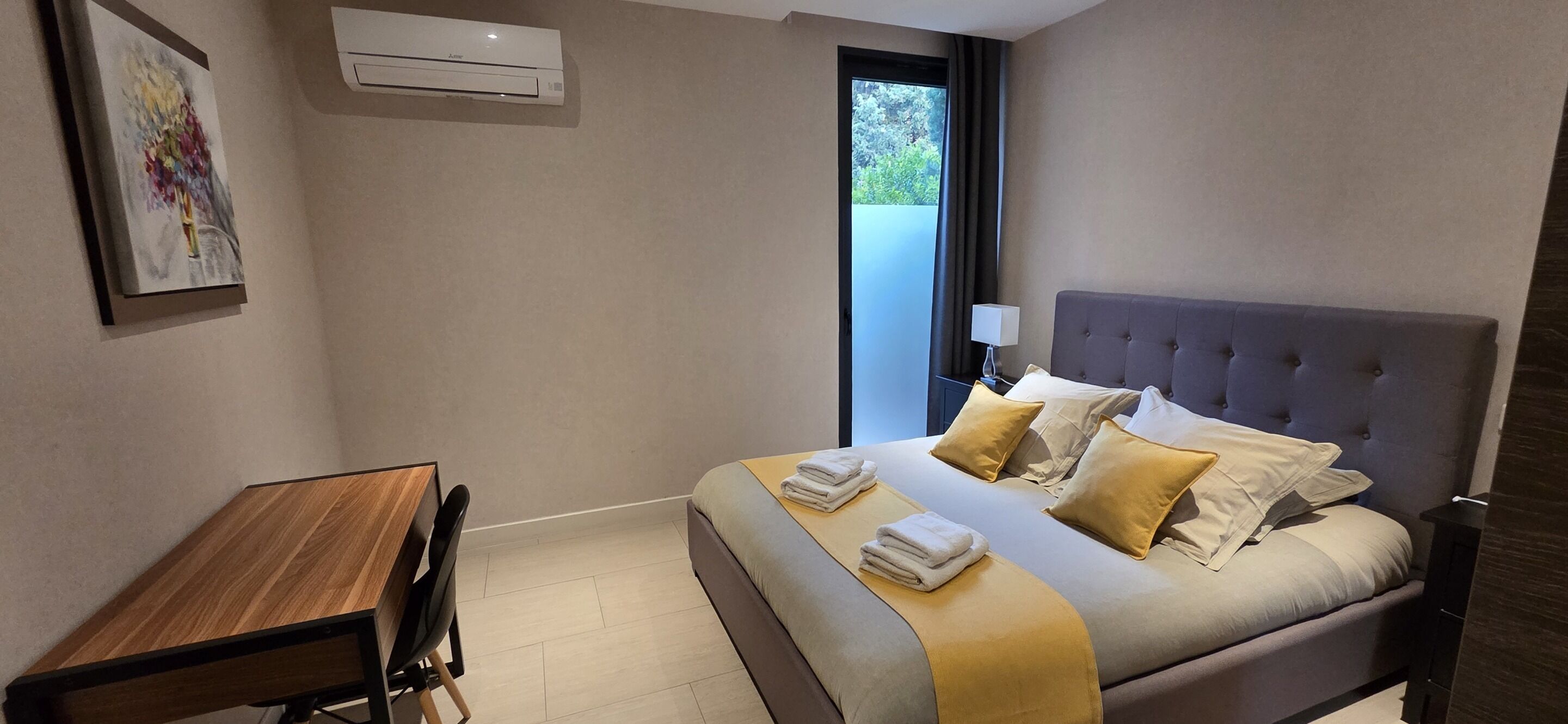 A modern hotel room with a bed, bedside table, chair, and a window with a view.