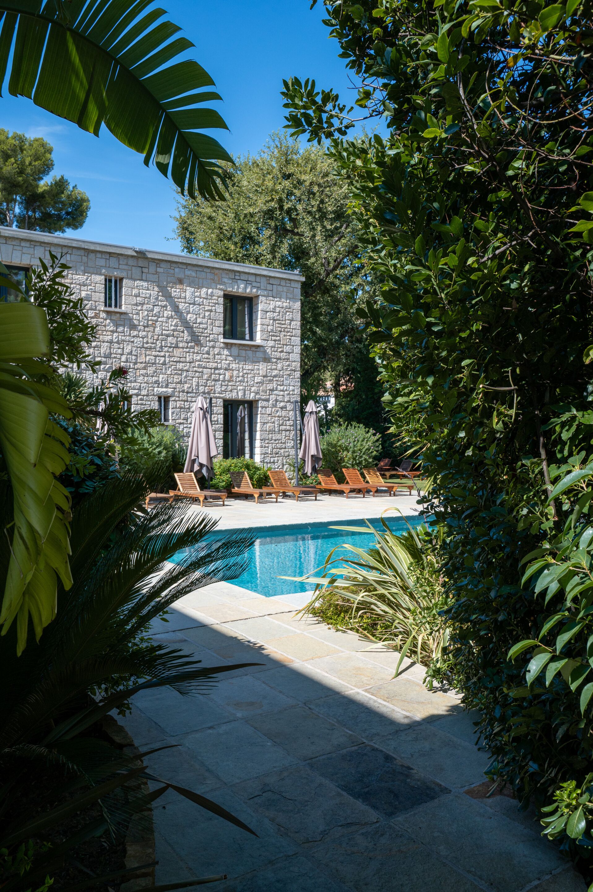 A stone building with a swimming pool, surrounded by lush greenery and outdoor seating.