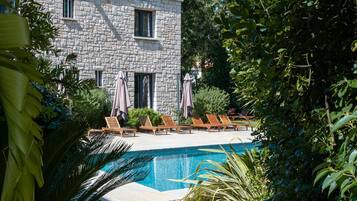 A stone building with a swimming pool, surrounded by lush greenery and outdoor seating.
