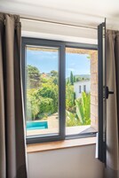 A window with a view of a swimming pool, greenery, and a building.