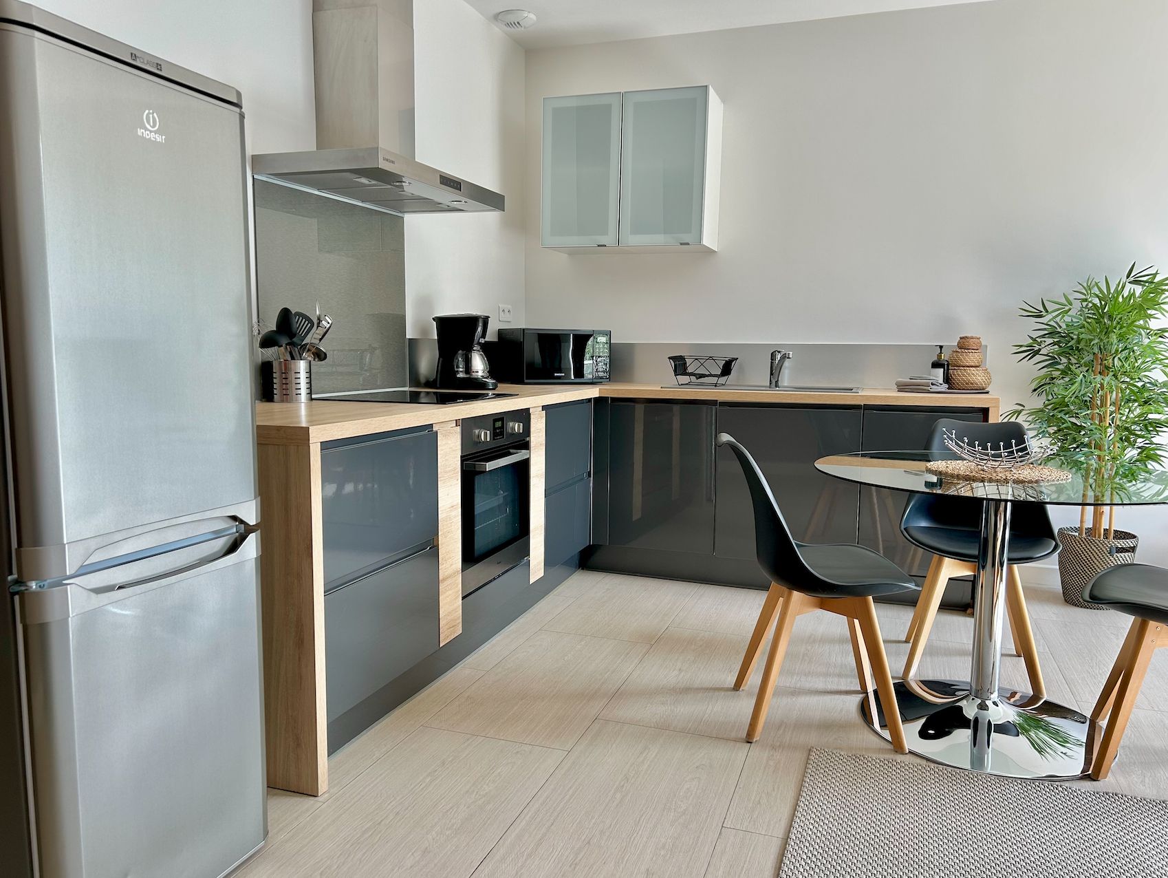 Een moderne keuken met een roestvrijstalen koelkast, een inbouwoven en een magnetron. Er is een eethoek met een ronde tafel en stoelen.