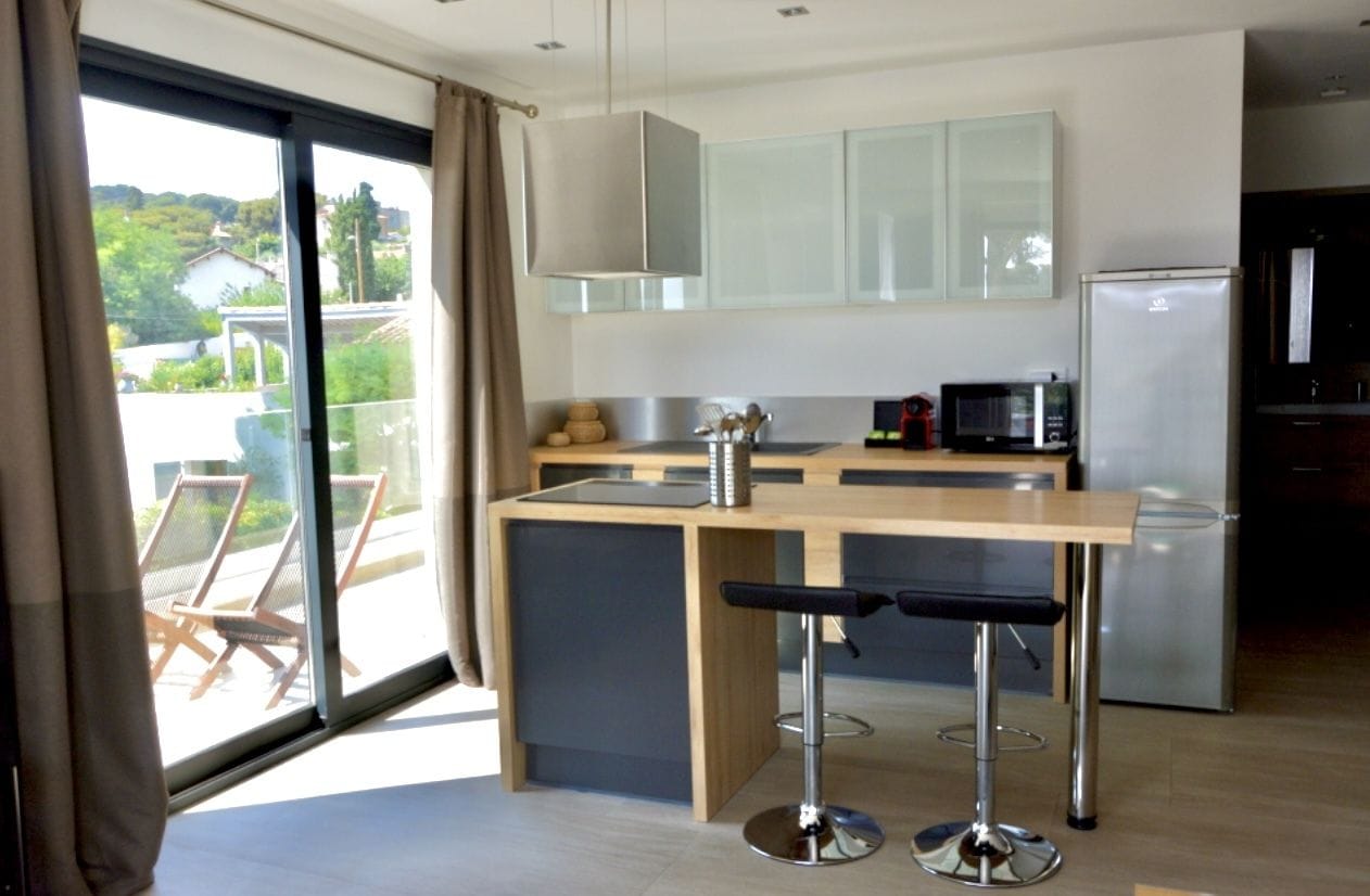 A modern kitchen with a central island, bar stools, a refrigerator, and a microwave.
